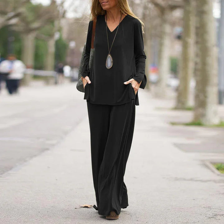 Woman walking outdoors in black long-sleeve V-neck top and wide-leg pants with pendant necklace
