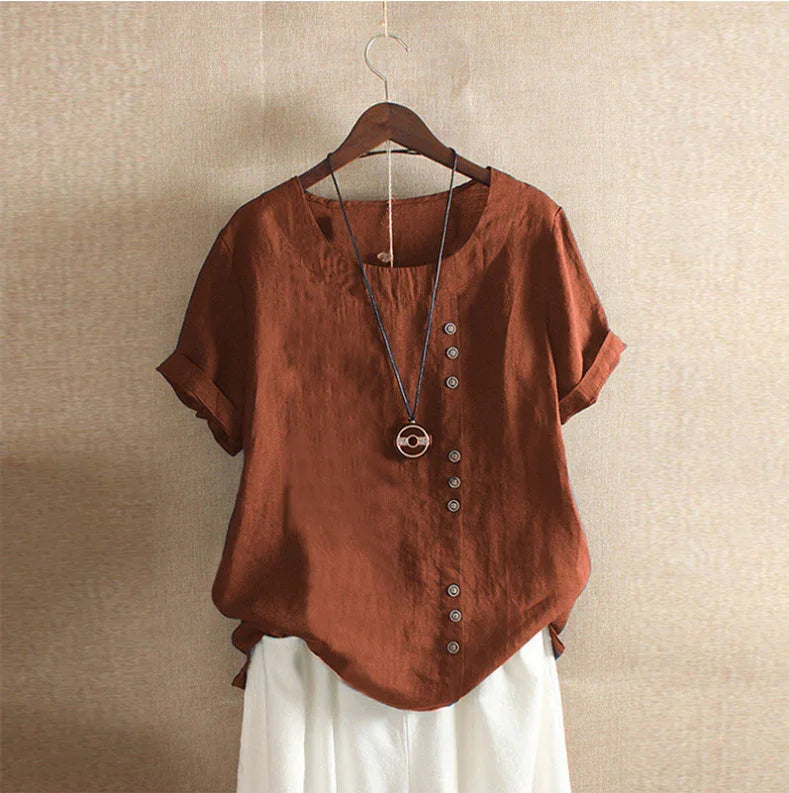 Rust brown short sleeve blouse with button details and pendant necklace on wooden hanger
