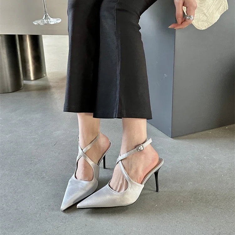 Woman wearing silver pointed toe stiletto heels with criss-cross ankle straps and black cropped pants indoors