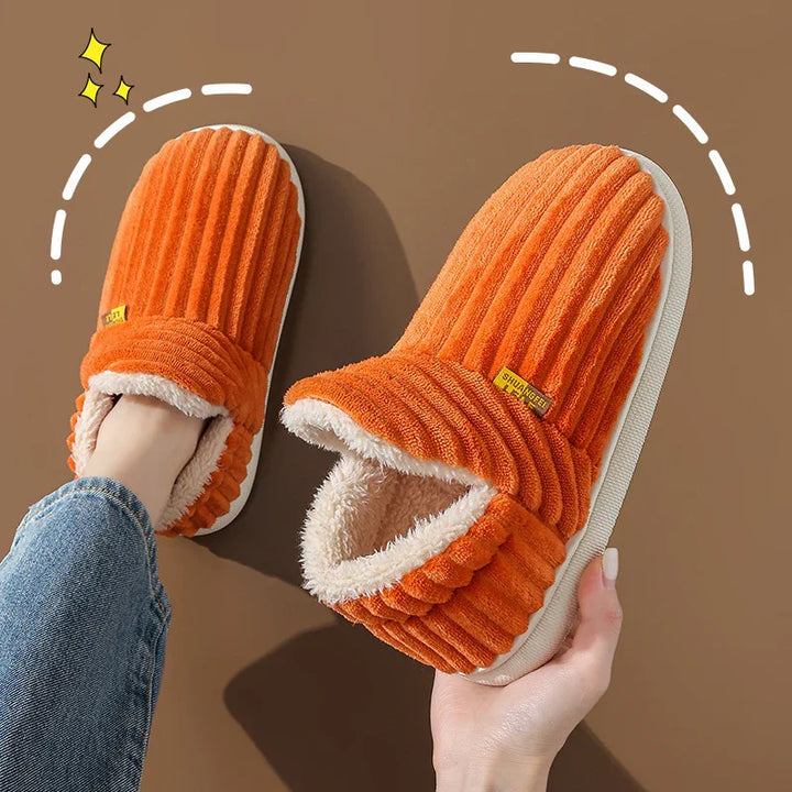 Orange ribbed corduroy indoor slippers with plush lining and white soles on brown background