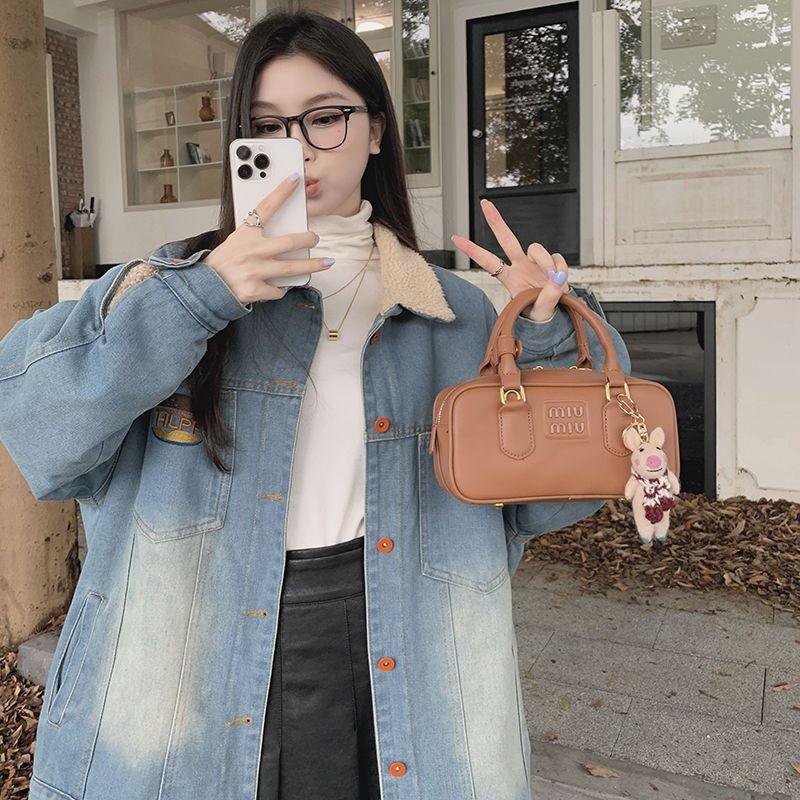 Young woman in denim jacket and glasses taking selfie, holding brown Miu Miu handbag with keychain