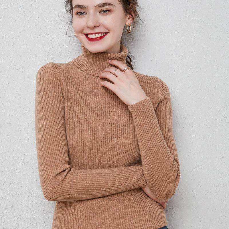 Smiling woman wearing a brown ribbed turtleneck sweater with gold hoop earrings and rings