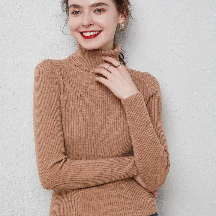 Smiling woman wearing a brown ribbed turtleneck sweater with gold hoop earrings and rings