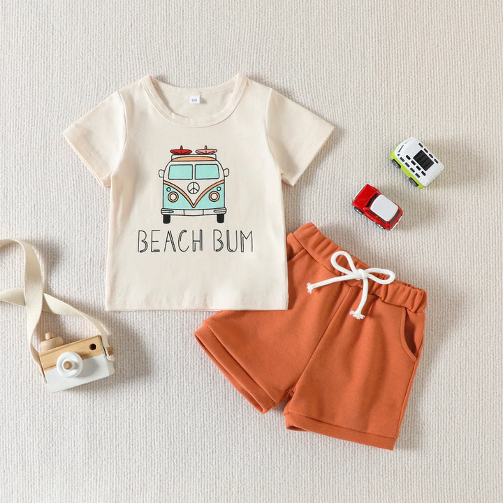 Toddler summer outfit with beige Beach Bum t-shirt and orange shorts on textured background