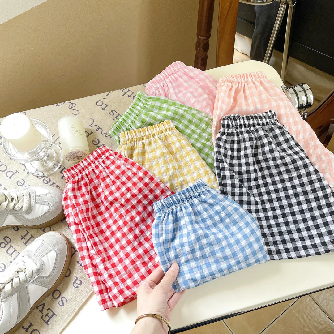Collection of colorful gingham checkered elastic waist shorts in pink, peach, green, yellow, black, red, and blue on a white chair