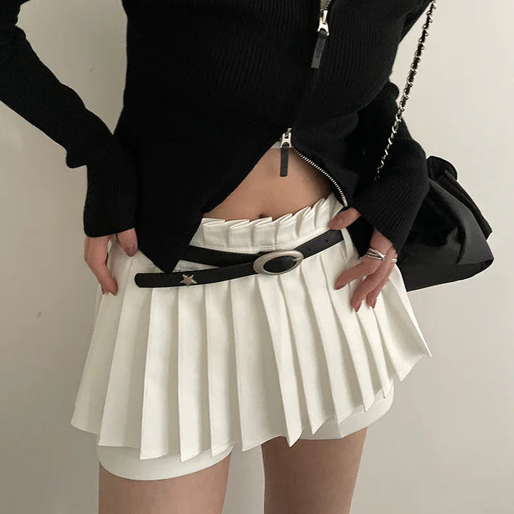 Woman wearing white pleated mini skirt with black belt and black zip-up sweater holding black purse