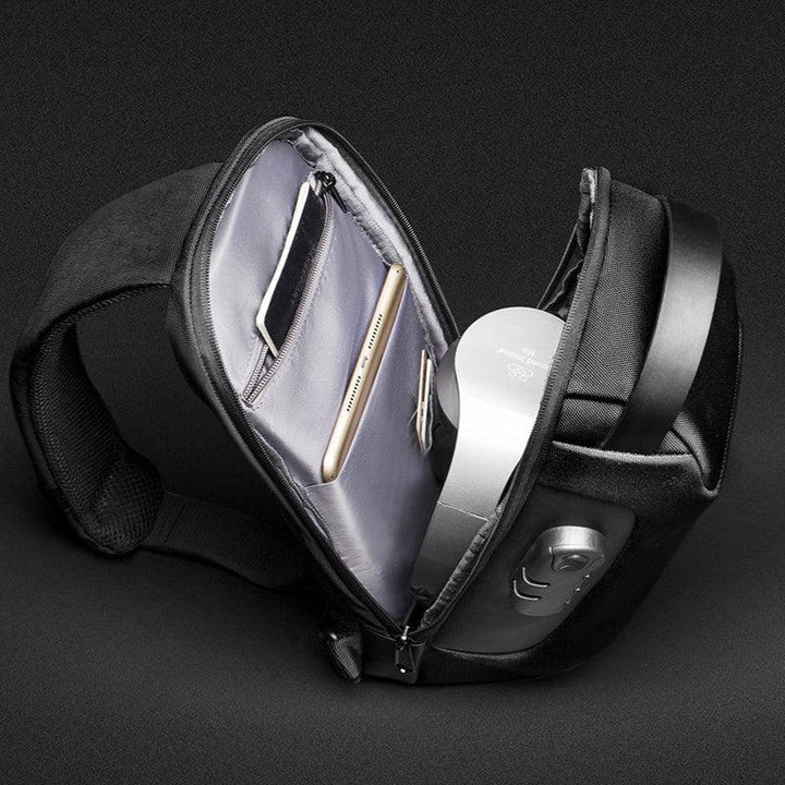 Black sling bag open to reveal organized compartments with smartphone, tablet, and metallic headphones