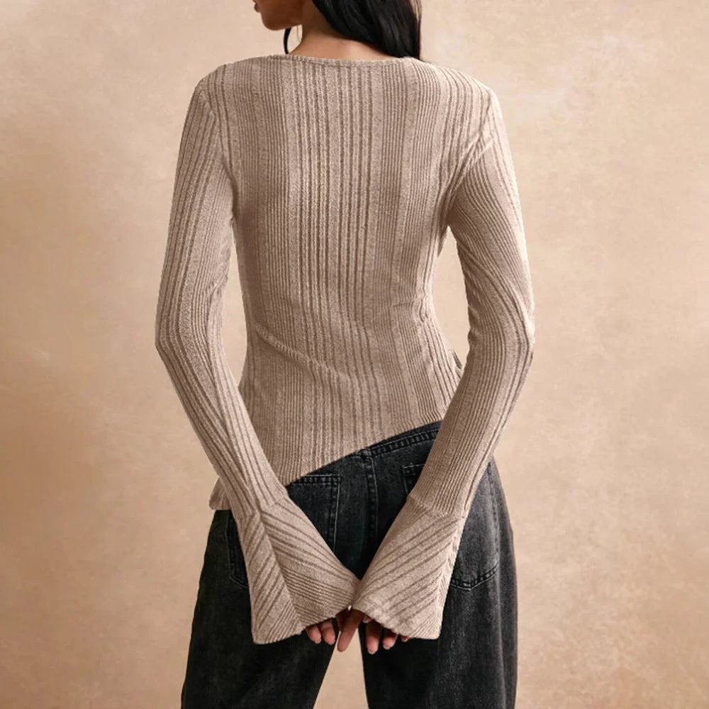 Back view of woman wearing beige ribbed knit sweater with flared cuffs and black denim jeans