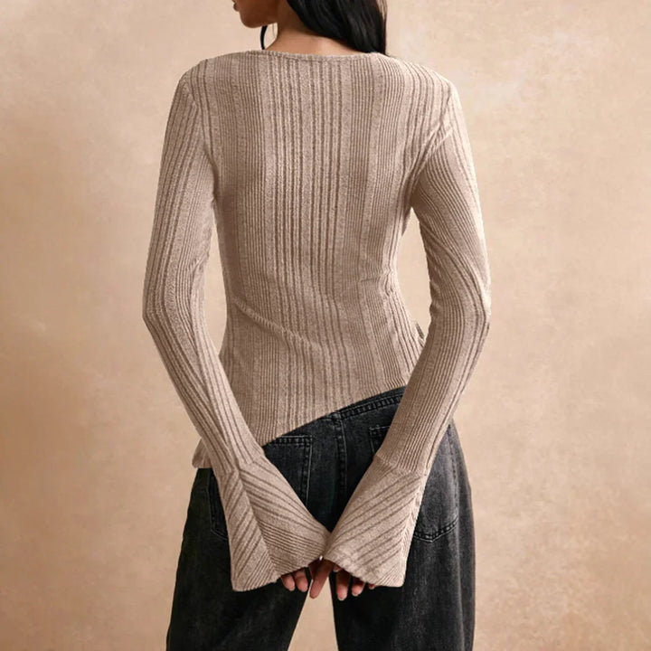 Back view of woman wearing beige ribbed knit sweater with flared cuffs and black denim jeans