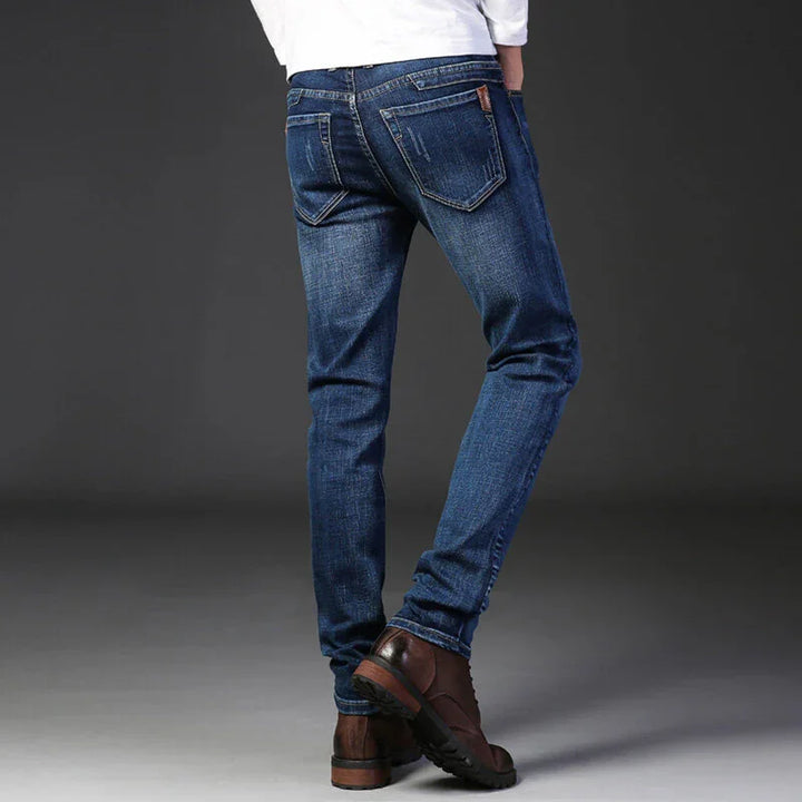 Rear view of person wearing slim fit blue jeans and brown leather boots on gray background
