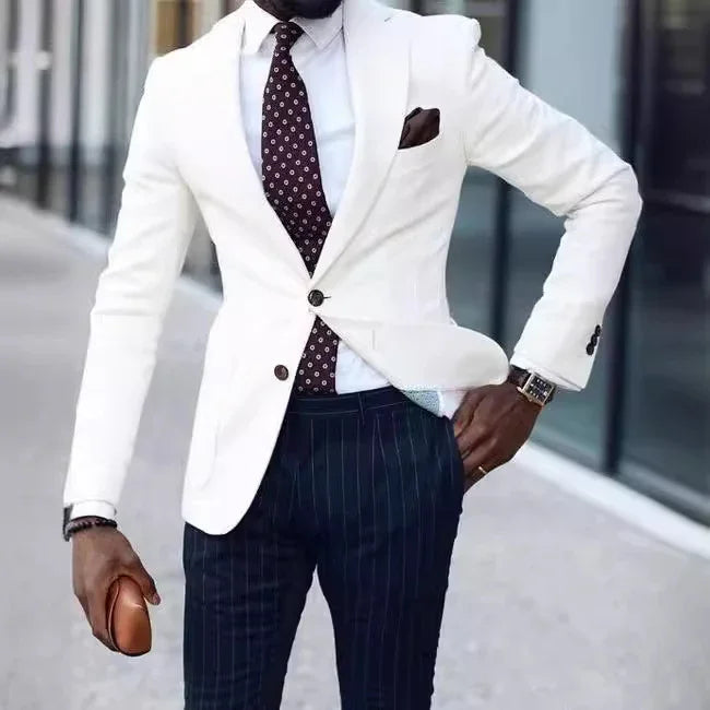Man in white blazer, patterned tie, navy pinstripe pants, holding brown clutch outdoors