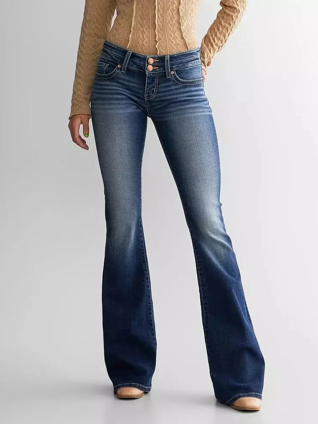 Woman wearing blue faded bootcut jeans and beige cable knit sweater against white background