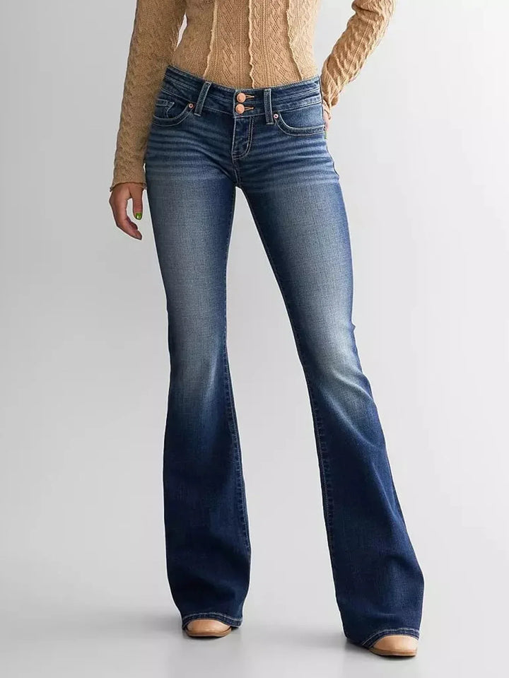 Woman wearing blue faded bootcut jeans and beige cable knit sweater against white background