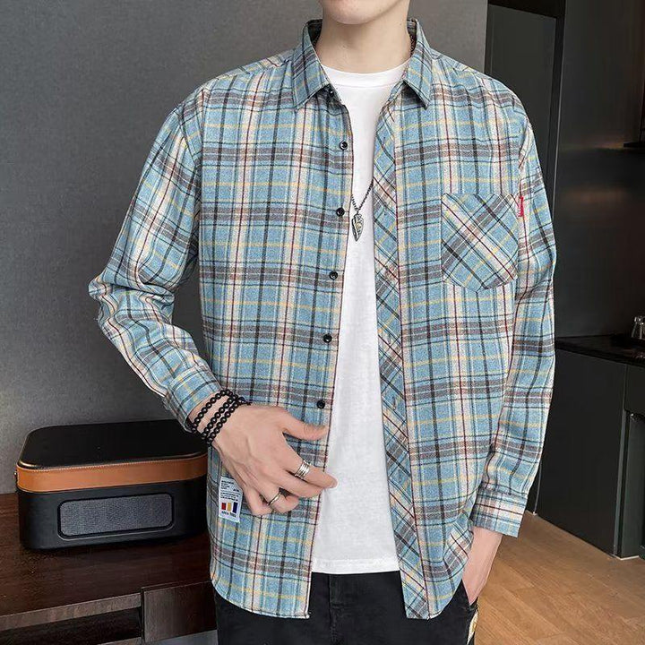 Man wearing blue plaid button-up shirt over white T-shirt with black pants indoors
