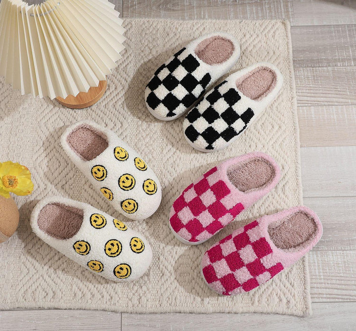 Three pairs of cozy indoor slippers with smiley faces and checkered patterns on a textured cream rug