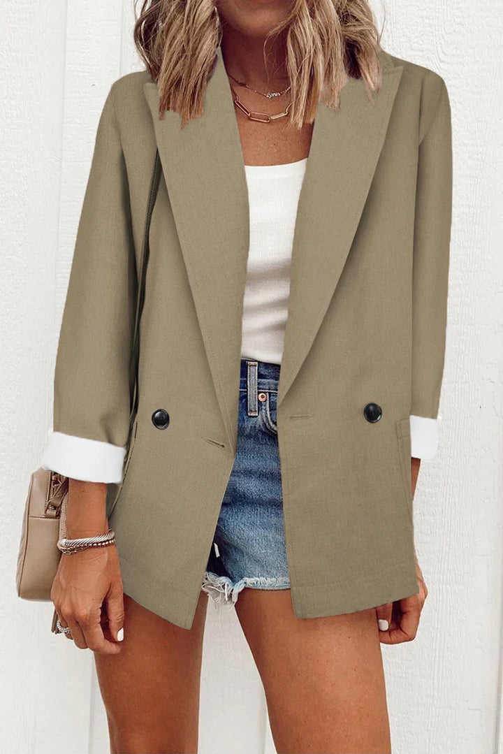 Woman wearing khaki double-button blazer with white cuffs, white top, denim shorts and beige handbag