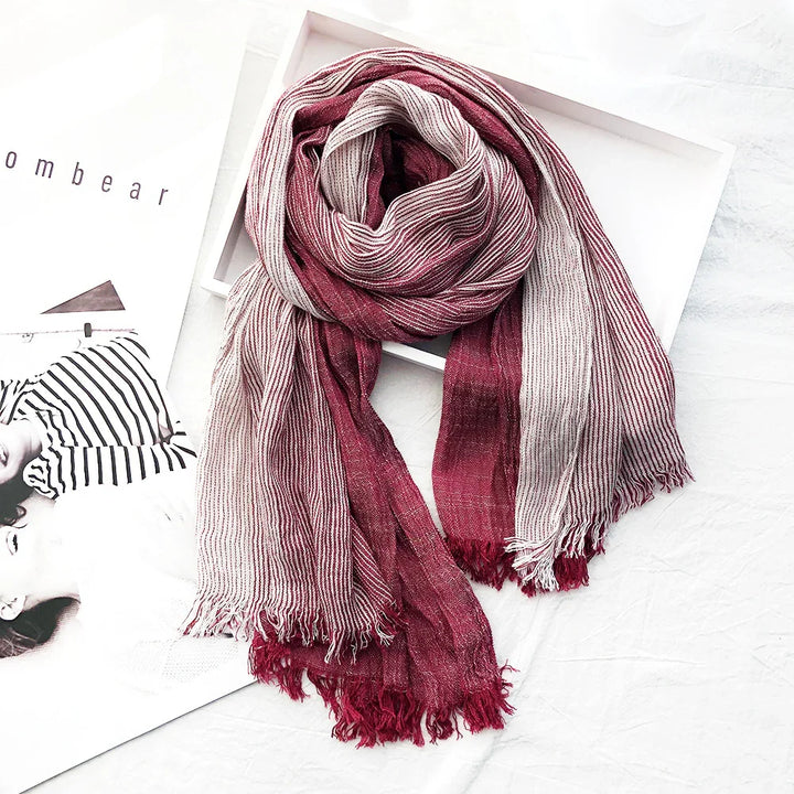 Striped red and white lightweight scarf with fringed ends on white surface with magazine