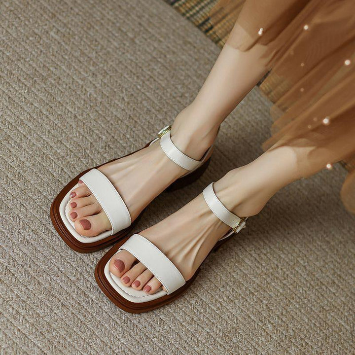 feet wearing white ankle-strap sandals with square brown soles on textured carpet