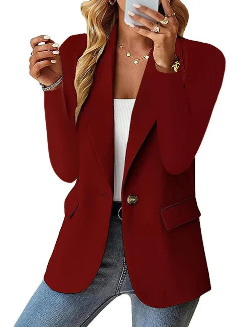 Woman wearing red blazer with single button, white top, and blue jeans holding phone