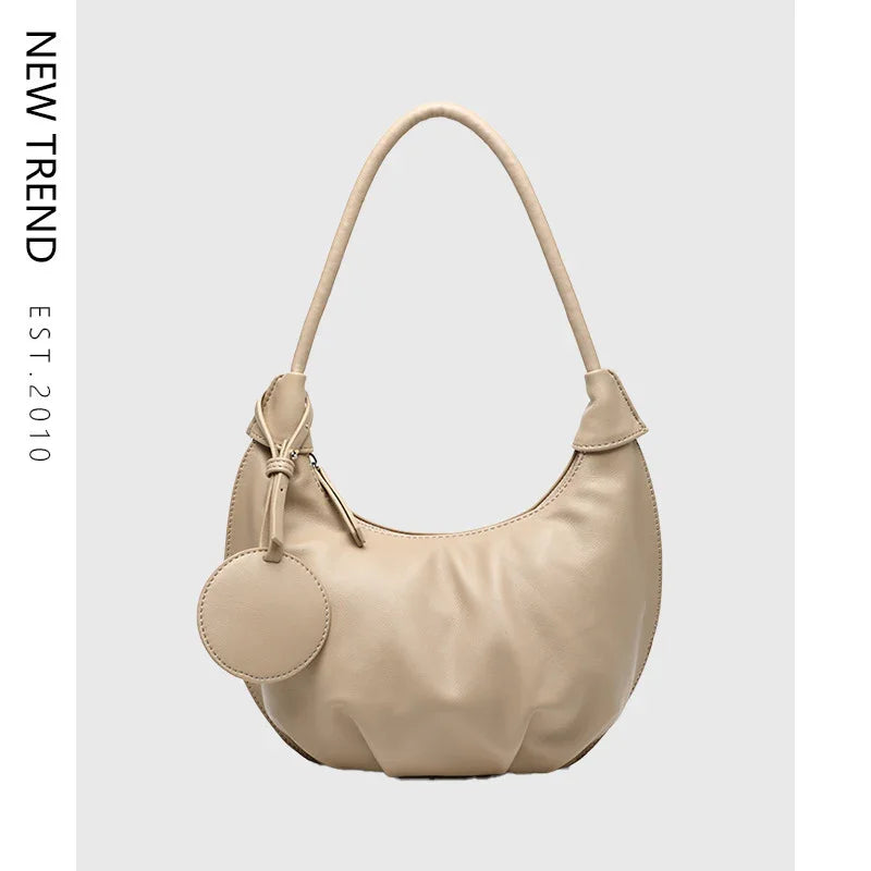 Beige crescent shoulder bag with round pouch and minimalist design on gray background