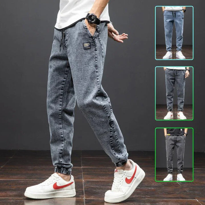Man wearing stylish grey jogger jeans with elastic cuffs and white Nike sneakers on wooden floor