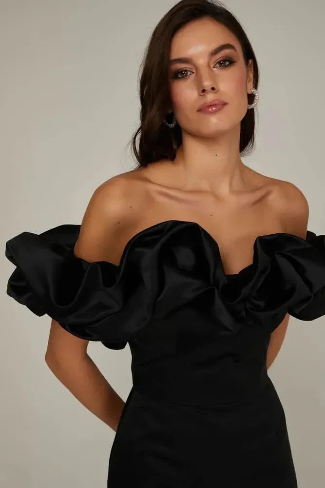 Woman wearing an elegant off-shoulder black satin dress with dramatic ruffled sleeves and hoop earrings