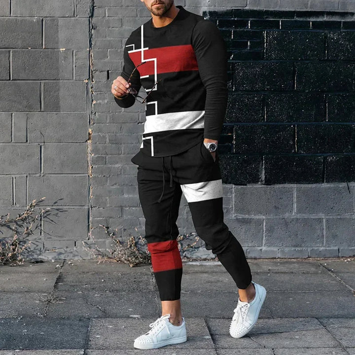 Man wearing black tracksuit with red and white geometric stripes and white sneakers against gray brick wall
