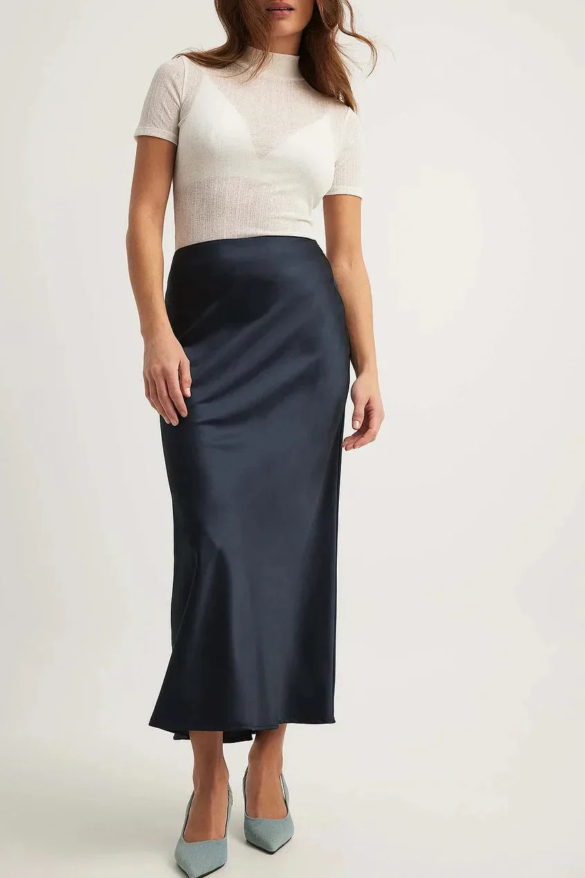 Woman wearing a white short-sleeve fitted top and a navy blue satin midi skirt with light blue pointed heels