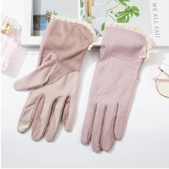 Pair of elegant pink fabric gloves with lace trim and white polka dots on a white surface with decor