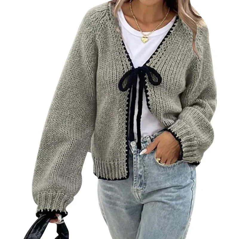 Woman wearing grey knit cardigan with black trim over white top and light wash jeans, holding black bag