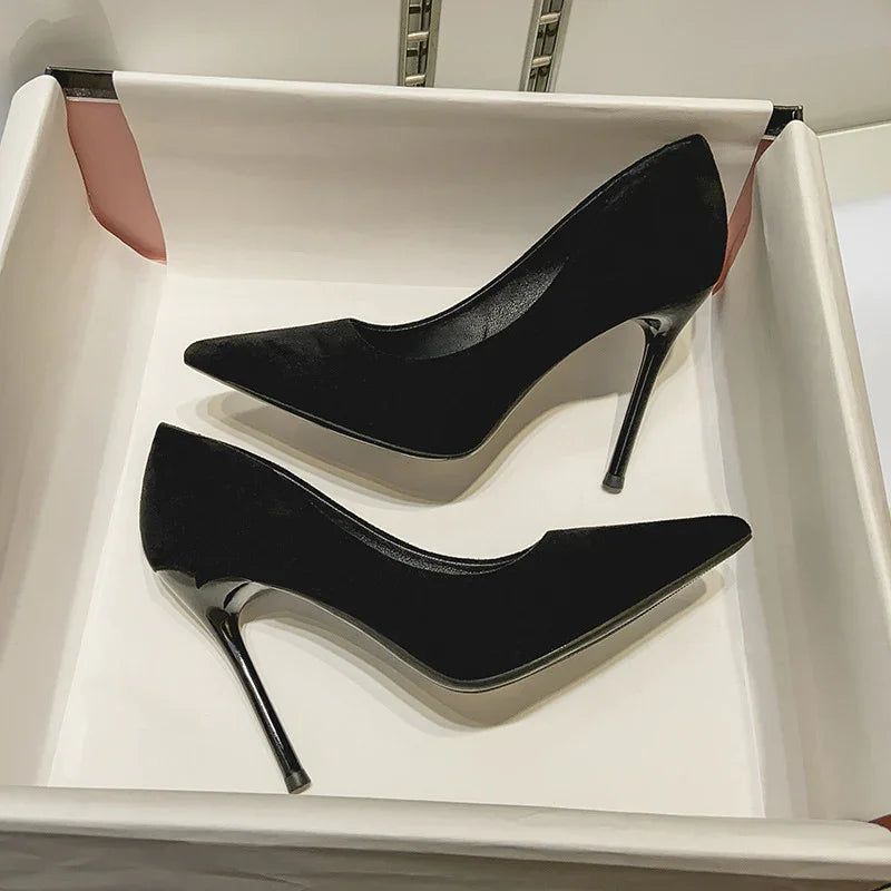 Pair of elegant black velvet stiletto heels with pointed toes in a white box