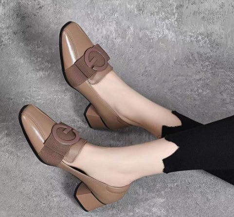 Brown block heel shoes with elastic strap and circular buckle worn with black pants on gray floor