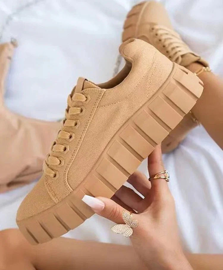 Close-up of beige chunky platform sneakers held by hand with butterfly ring and long nails