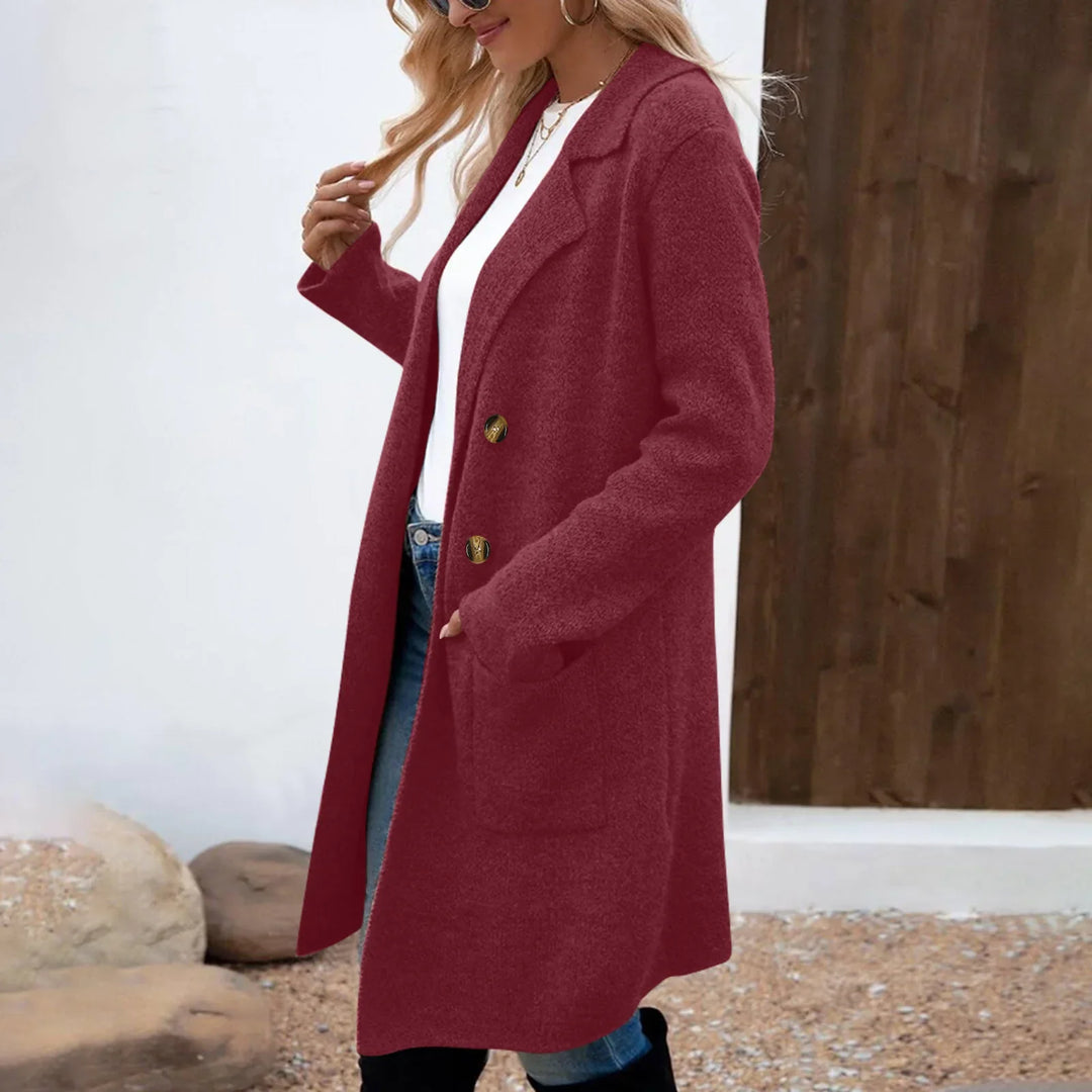 Woman wearing a long burgundy wool coat with gold buttons, white shirt, blue jeans, and sunglasses outdoors