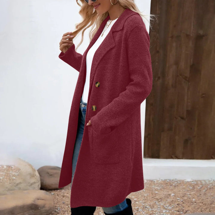 Woman wearing a long burgundy wool coat with gold buttons, white shirt, blue jeans, and sunglasses outdoors