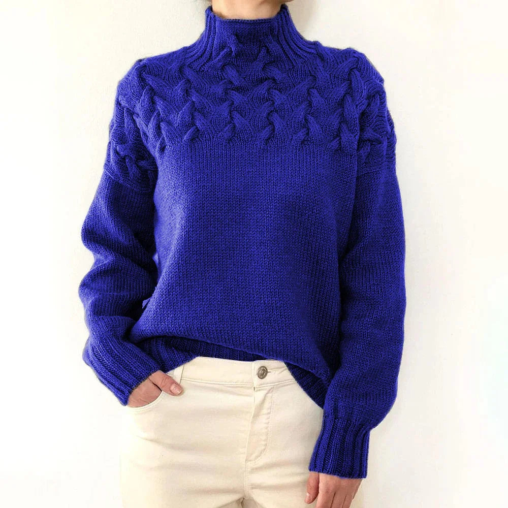 Woman wearing a blue cable knit turtleneck sweater with long sleeves and cream pants