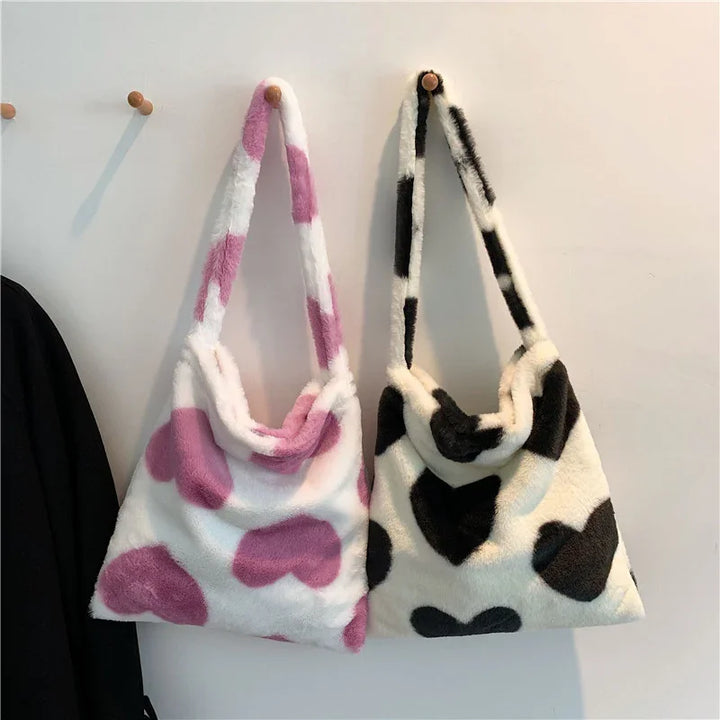 Two fluffy faux fur handbags with heart patterns hanging on wall hooks, one pink and white, one black and white