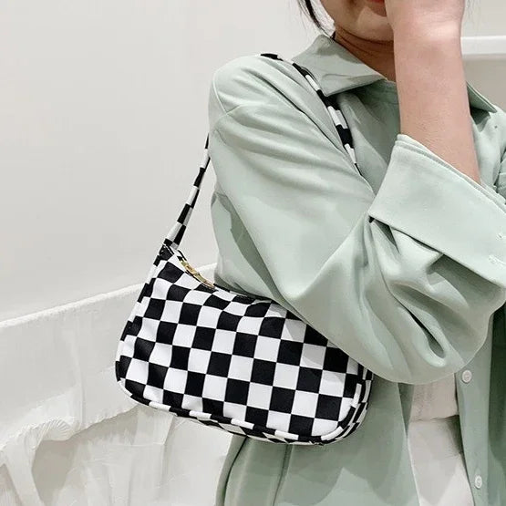 Person wearing a light green shirt holding a black and white checkered shoulder bag indoors