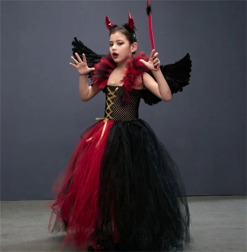 Child dressed in red and black devil costume with wings and horn headband against plain background