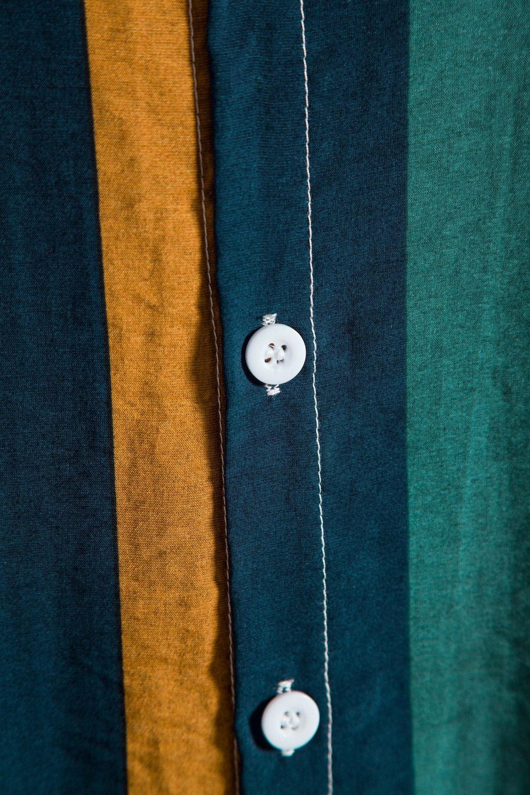Close-up of a striped shirt with vertical mustard, navy blue, and teal stripes and white buttons