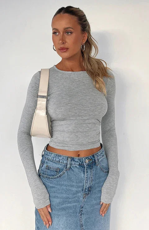 Woman wearing a fitted grey long-sleeve crop top and blue denim skirt with a cream shoulder bag