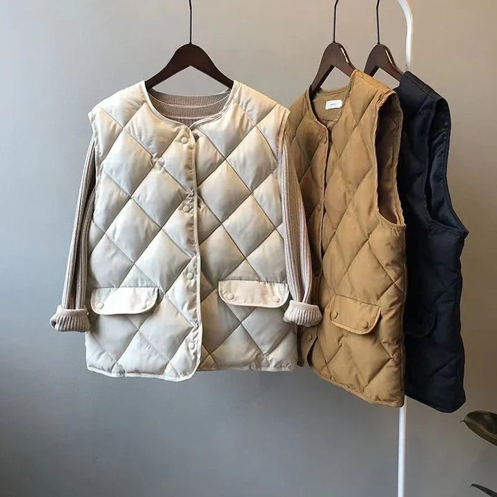 Three quilted sleeveless vests in beige, brown, and black hanging on wooden hangers against a gray wall