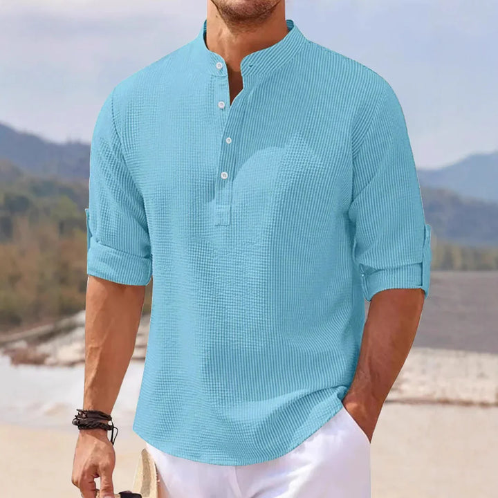 Man wearing light blue textured casual shirt with mandarin collar and rolled-up sleeves at beach