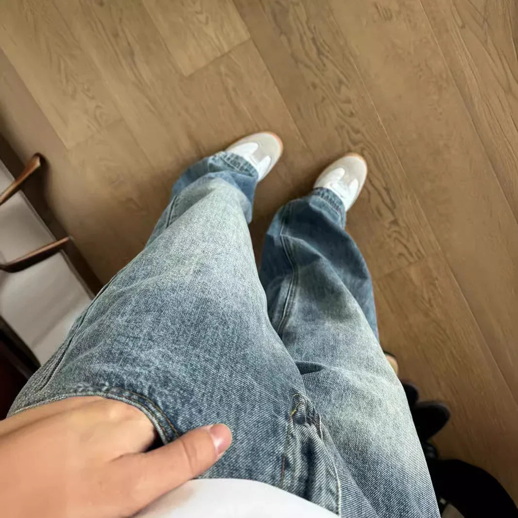 Person wearing light blue denim jeans and white sneakers standing on wooden floor