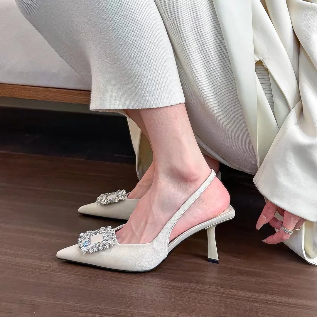 Woman wearing elegant beige slingback heels with rhinestone buckles on wooden floor