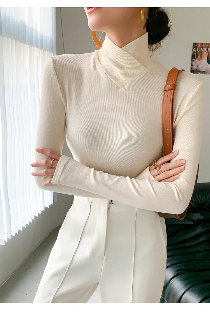 Woman wearing cream beige ribbed knit long sleeve top with cross neck and high waist white pants indoors