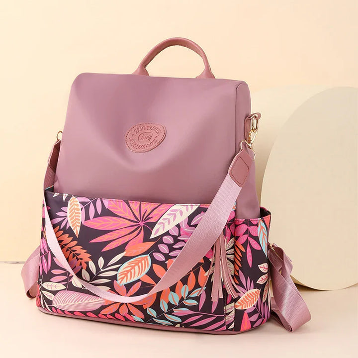 Pink and floral patterned backpack with adjustable shoulder strap and top handle on beige background