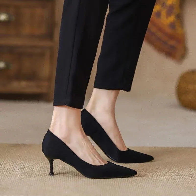 Woman wearing black pointed-toe kitten heel pumps paired with black cropped pants on beige carpet