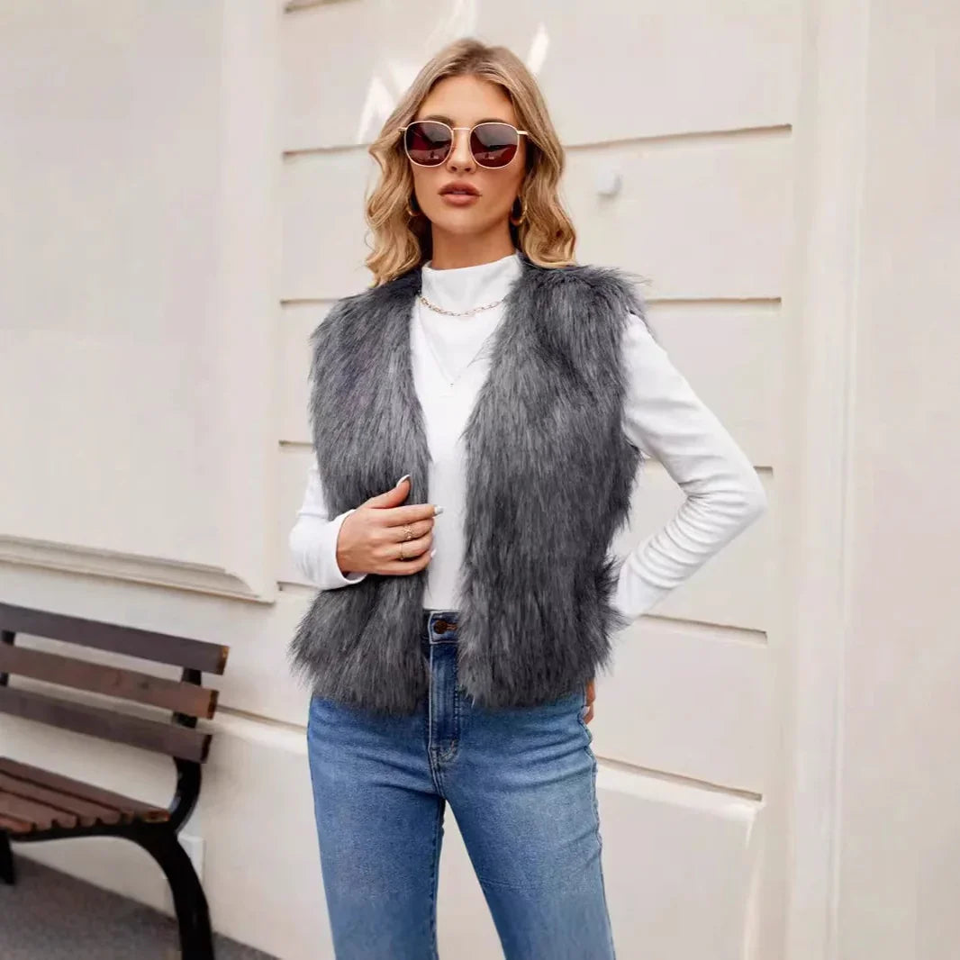 Fashionable woman wearing gray faux fur vest, white long sleeve top, and blue jeans outdoors