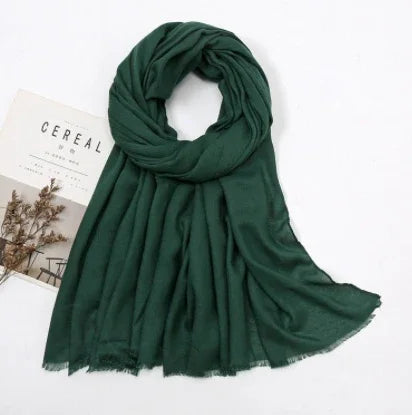 Dark green lightweight scarf with fringed edges on white background, next to CEREAL magazine and dried flowers